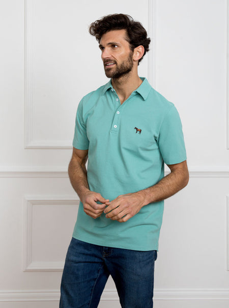 Man wearing avocado green polo shirt in 100% cotton with Newmarket 875 horse logo embroidered on the front.